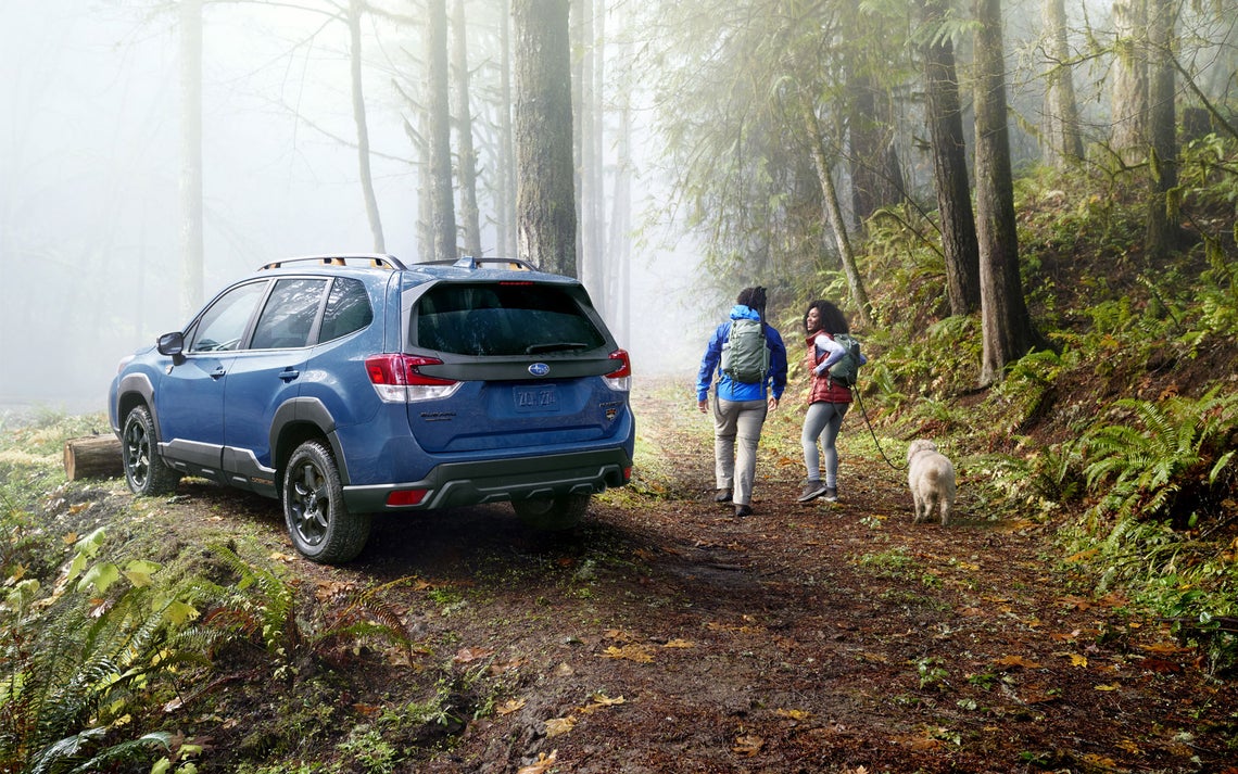 COUPLE WALKING DOG NEXT TO PARKED BLUE 2022 FORESTER WILDERNESS